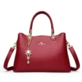 Elegante rote Lederhandtasche mit Tragegriffen, Schultergurt und floralem Anhänger. - Burgunderrot