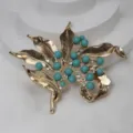 Vue détaillée d'une broche feuille vintage dorée ornée de perles turquoise et de strass. - Vert