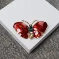 Gros plan detaille de la broche papillon en emai rouge vintage avec strass verts et champagne. - Rouge