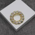 Gros plan détaillé d'une broche vintage en chaîne dorée et perles au design creux élégant. - Broche / Or