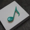 Close-up detail of the turquoise enamel music note brooch, showing fine gold metal trim. - Turquoise Green