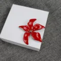Gros plan d'une broche fleur en émail rouge sur boîte blanche, détail de design élégant. - Rouge