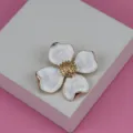 Vue en gros plan d'une broche florale en métal vintage à pétales blancs et étamines d'or. - Blanc