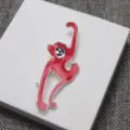 Vue détaillée d'une broche élégante en émail rouge singe à longs bras sur un support blanc. - Singe Rouge