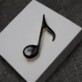Detailed close-up view of a black enamel musical note brooch with elegant gold trim. - Black