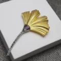 Vue rapprochée de la broche feuille de ginkgo élégante en or mat et cristaux étincelants. - Broche