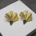 Gros plan de boucles d'oreilles feuille de ginkgo en or mat vintage et strass foncés. - Boucles d'oreilles clous