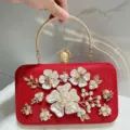 Red pearl evening bag detail, featuring metallic round handle and shell floral decoration. - Red