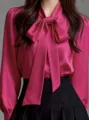 Close-up detail of the elegant satin pink blouse with a large bow tie neck design. - Rose Red