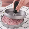 Detail shot of aluminum burger press with black plastic handle shaping meat patty. - Standard Type
