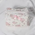Quilted floral cosmetic bag detail showcasing lace trim, zipper, and cute bow pearl pendant. - Quilted Lace Cosmetic Bag + Pink Double Pearl Bow