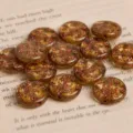 Close-up detail of amber glass coin beads with copper star and moon patterns on a book page. - Amber Rose Gold