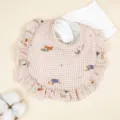Close-up detail view of newborn cotton gauze baby bib featuring cute plaid pattern and ruffles. - Plaid Puppy