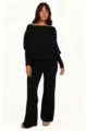 Detalle de cerca del suave top negro de punto con hombros descubiertos y pantalón acampanado. - S / Negro