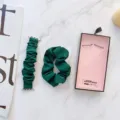 Detailansicht des dunkelgrünen Scrunchie-Uhrenarmbands mit passendem Haargummi und Geschenkbox. - Einfarbig Smaragdgrün