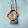 Detailed shot of bright orange protective smartwatch case hanging on a minimalist grey wall bag. - Orange