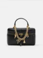 Detailed view of black structured vanity box bag with gold chain charms and top handle. - Black