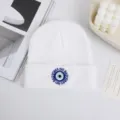 Dettaglio del berretto in maglia bianca con ricamo dell'occhio malvagio blu e design elegante. - Stampa Occhio Bianco