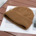 Close-up detail of a cozy brown knitted beanie resting on a styled magazine surface. - One Size (High Elasticity) / Camel