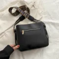 Schwarze Leder Umhängetasche mit breitem Monogramm-Gurt und Reißverschlusstasche - Schwarz