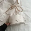 Beige Beuteltasche mit Kettengurt und schickem Dreiecksaufnäher vorne, elegant und vielseitig. - Weiß