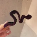 Primo piano dettagliato della molletta per capelli con strass viola scuro e design a onde irregolari. - Viola