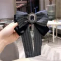 Detailed close-up of a dark blue herringbone ribbon bow brooch with crystal gemstone center. - Navy Blue