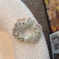 Primo piano di un elastico per capelli a pois bianchi in tulle con perla elegante e bordo a volant. - Stile Perla Tonda / Bianco avorio