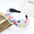 Dettaglio in primo piano della fascia per capelli in tessuto largo con stampa alfabeto colorata. - Bianco