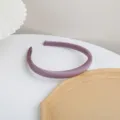 Detail shot of a sleek purple satin headband on a clean white tabletop with minimalist props. - Violet