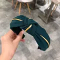 Primer plano detallado de una diadema de tela verde oscuro con ribete dorado y nudo. - Verde Oscuro