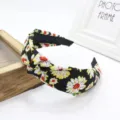 Primer plano detallado de una diadema vintage con nudo floral negro y patrones de margaritas amarillas. - Negro