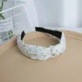 Primer plano detallado de una diadema ancha de tela blanca con estampado floral, accesorio. - Verde