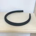 Detailed view of a simple black padded sponge headband placed on a wooden shelf. - Black