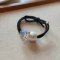 Primo piano di un elegante elastico per capelli nero con cristallo triangolare e perla. - Bianco