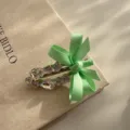 Primo piano di un dolce fermaglio per capelli a becco d'anatra verde chiaro con fiocco e strass. - Verde mela