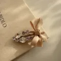Detail shot of a sweet rhinestone bow hair clip, elegant beige fabric accessory for women. - Beige