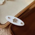 Primo piano di un fermaglio per capelli ovale bianco con fiore di perline e metallo. - Bianco