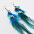 Detailopname van lange boho veren oorringen met antieke gouden bladhangers voor dames. - Meerblauw
