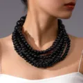 Gedetailleerde close-up van een meerlaagse zwarte houten kraalketting met handgemaakte textuur. - Zwart
