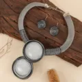 Close-up detail shot of a unique geometric statement necklace and spiral earrings set on rustic wood. - White