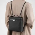 Detailed view of black leather backpack with silver lock and straps on model's back. - Black