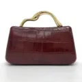 Vista dettagliata della borsa bordeaux con stampa coccodrillo e manico dorato di lusso. - Rosso