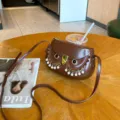 Detailed view of the brown leather owl saddle bag featuring pearl fringe and gold hardware. - Brown