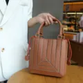 Brown PU leather small square handbag with geometric stitched design and orange side drawstrings. - Brown