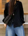 Detail view of the retro polka dot pleated crescent shoulder bag in street style setting. - Black