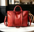 Detail shot of a red soft leather tote bag on white table in a cafe, showcasing texture. - Red