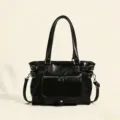 Black patent leather shoulder bag detail, featuring dual top handles and metal hardware. - Black