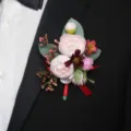 Nahaufnahme Detailansicht des eleganten künstlichen Rosen-Hochzeits-Ansteckers am schwarzen Revers. - Kamelie Ansteckblume