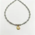 Detailed close-up of stainless steel beaded necklace featuring a stylish gold letter G pendant. - Letter G